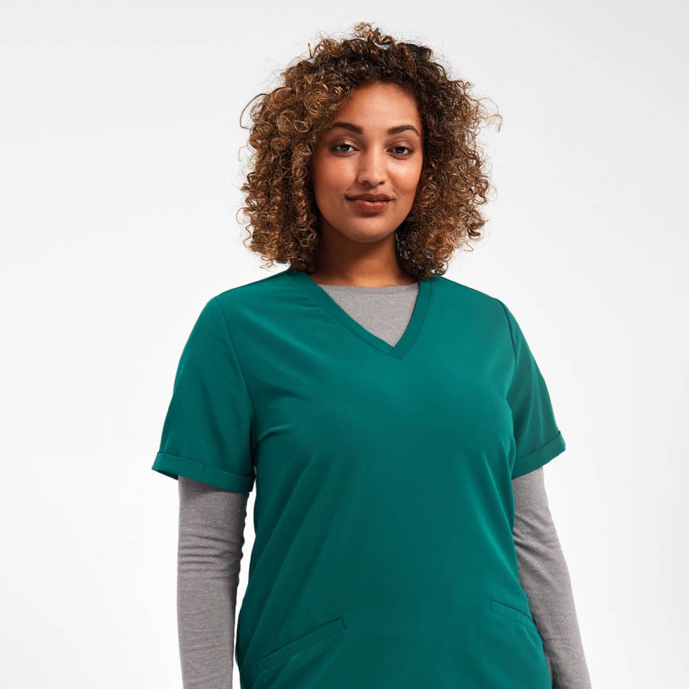 A woman with curly hair wearing the Onna by Premiers Clean Green V-neck medical scrub top over a long-sleeve grey underscrub