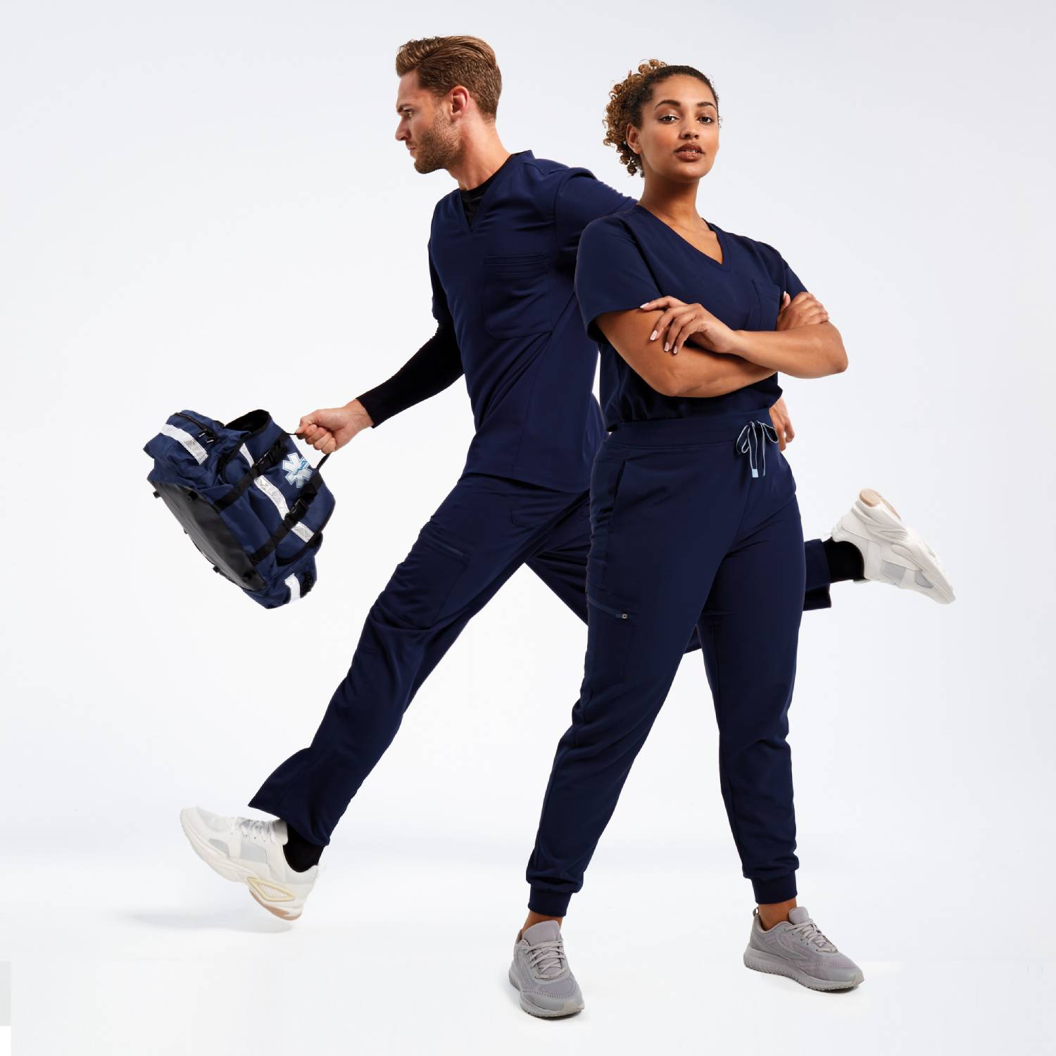 Two models wearing Onna by Premier navy blue medical scrubs; one standing confidently with arms crossed, while the other is in motion holding a medical-style backpack.