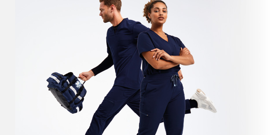 Two models wearing Onna by Premier navy blue medical scrubs; one standing confidently with arms crossed, while the other is in motion holding a medical-style backpack.