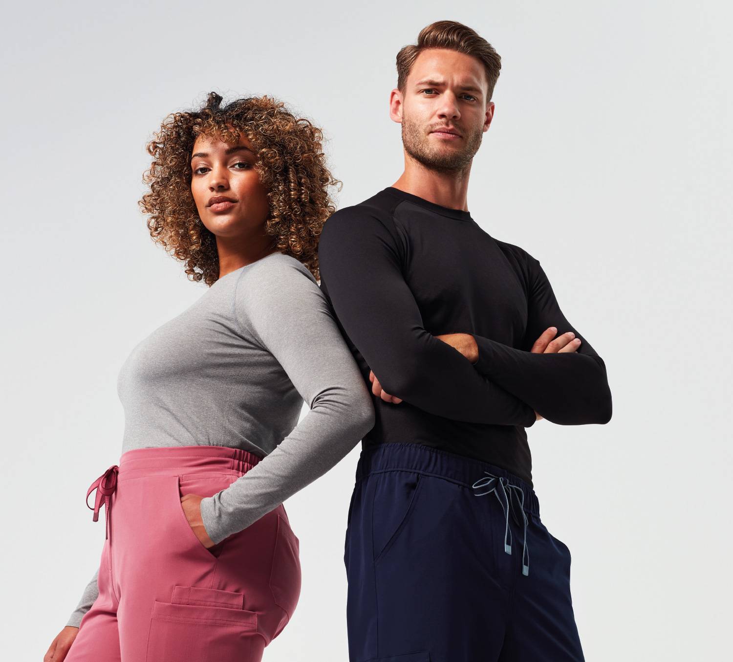 A woman and man standing back to back with arms crossed.Both wearing 