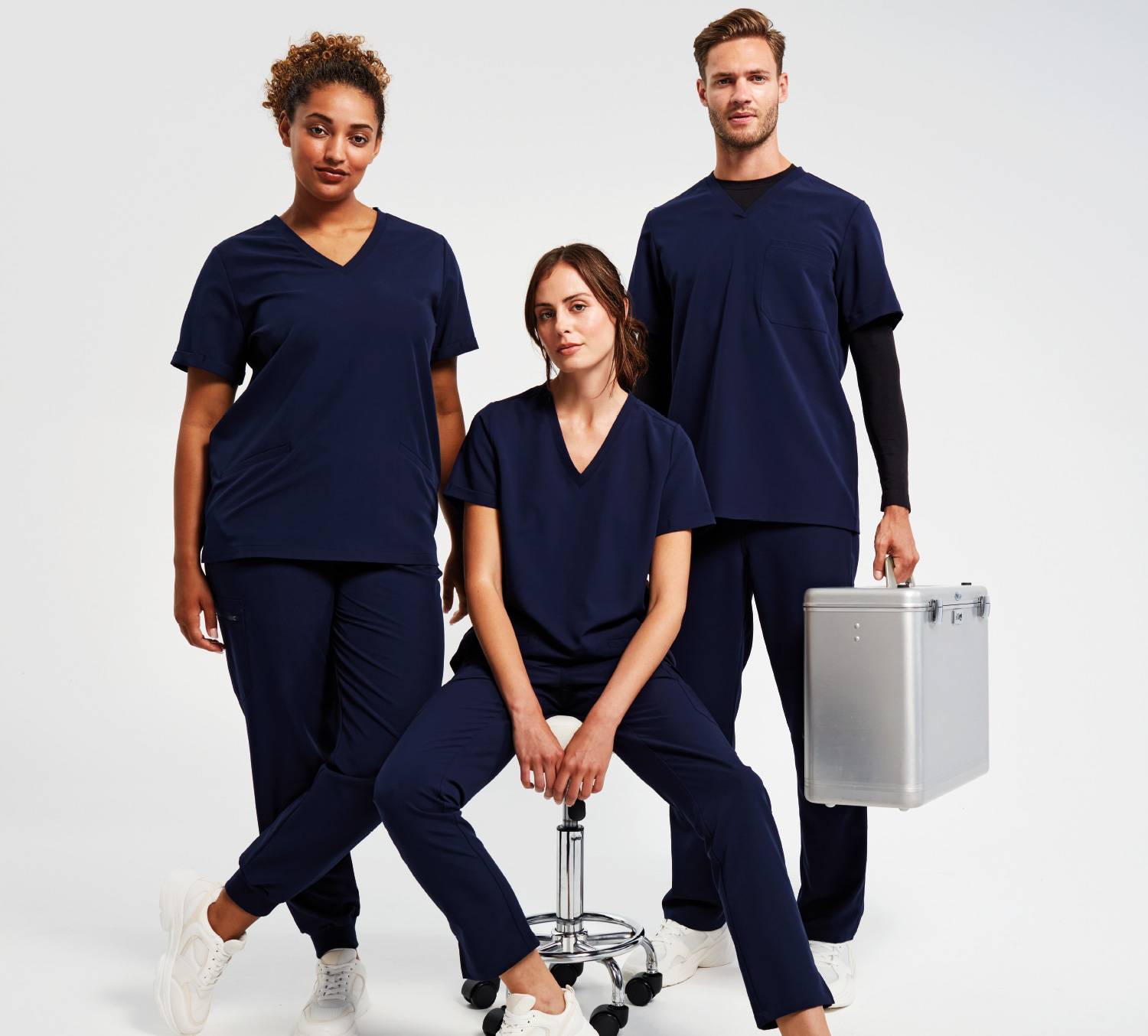 Two women and one man wearing Onna by Premier Action Navy Scrubs.The man is carrying a medical briefcase and one woman is sat down on a stool